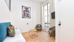 Uma sala de estar moderna com um sofá, duas poltronas estampadas, uma mesinha e uma janela grande com cortinas.