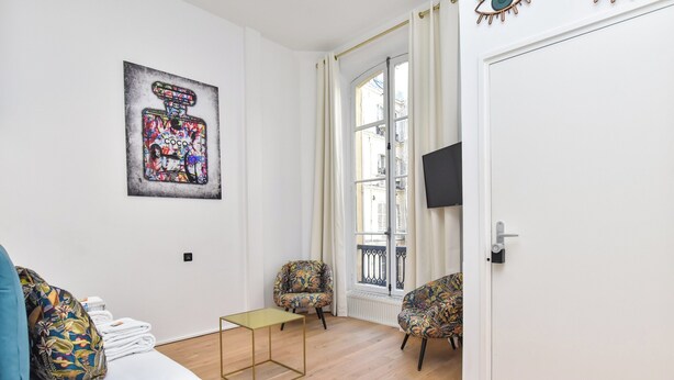 Uma sala de estar moderna com sofá, duas cadeiras estampadas, uma mesa pequena e uma janela grande com cortinas.
