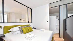 Quarto de hotel moderno com uma cama grande, cabeceira verde, espelho amplo e closet espaçoso.