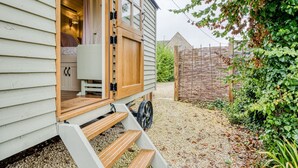 A small wooden house with a porch, a wheelbarrow, and a gravel path.