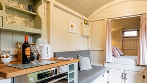 A compact kitchenette with a stove, a kettle, and a wine bottle.