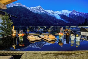 A dining table with a view of snow-capped mountains, a bottle of champagne, and various cheeses and bread. - Luxurious Chalet Peace & Love 10pers (Chamonix-Mont-Blanc)