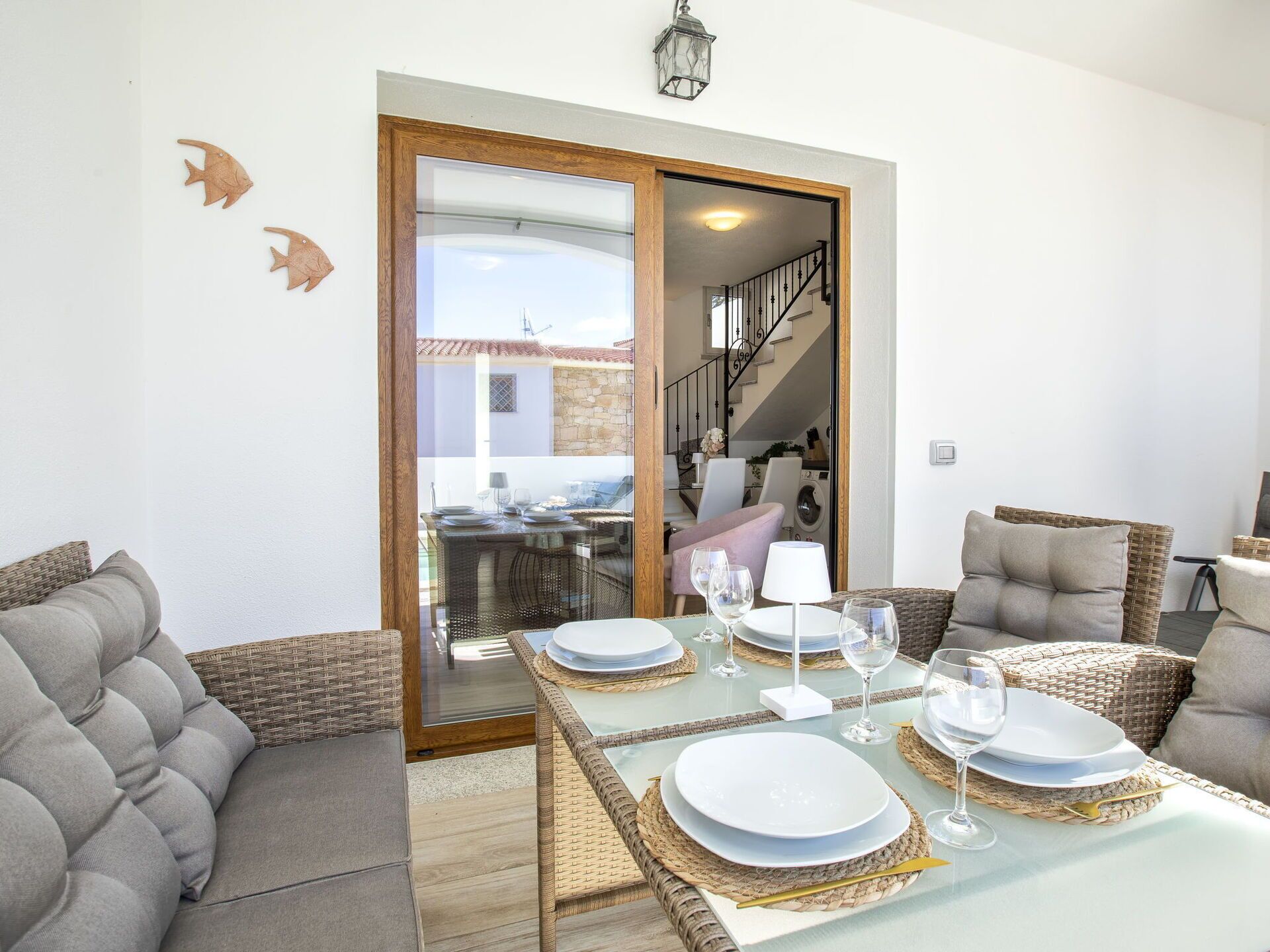 Un coin repas avec une table à plateau de verre, dressée pour quatre personnes, entourée de meubles en osier.