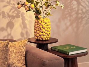 A room with a round wooden table, a vase of lemons, a green book, and a patterned pillow.
