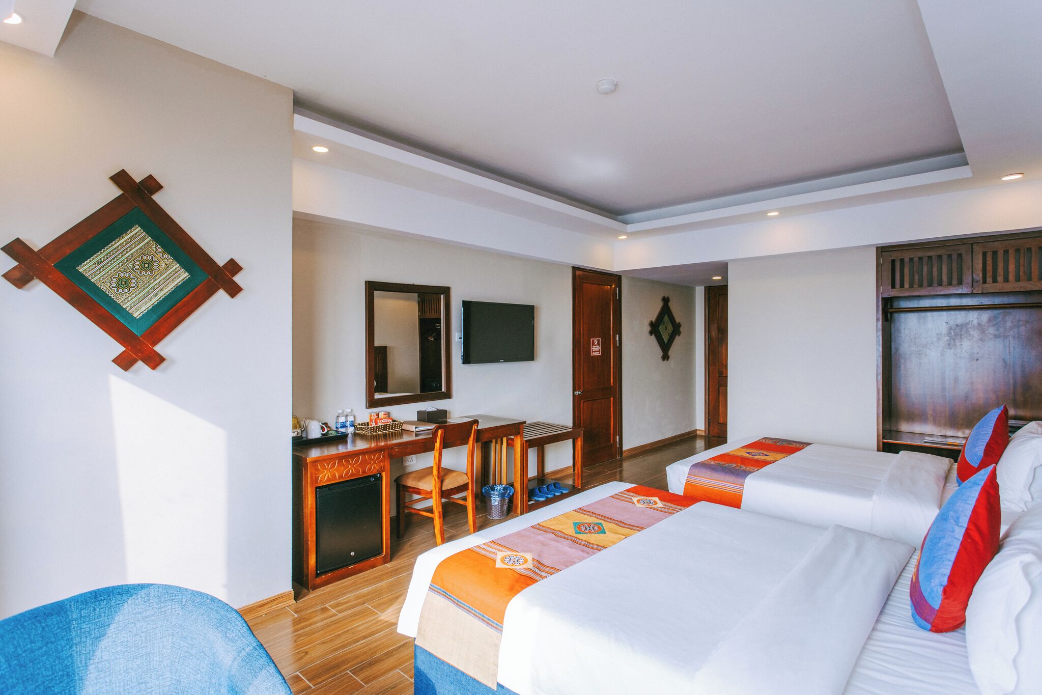 Ein Hotelzimmer mit zwei Betten, einem Schreibtisch, einem Stuhl, einem Fernseher und einem Holzschrank.