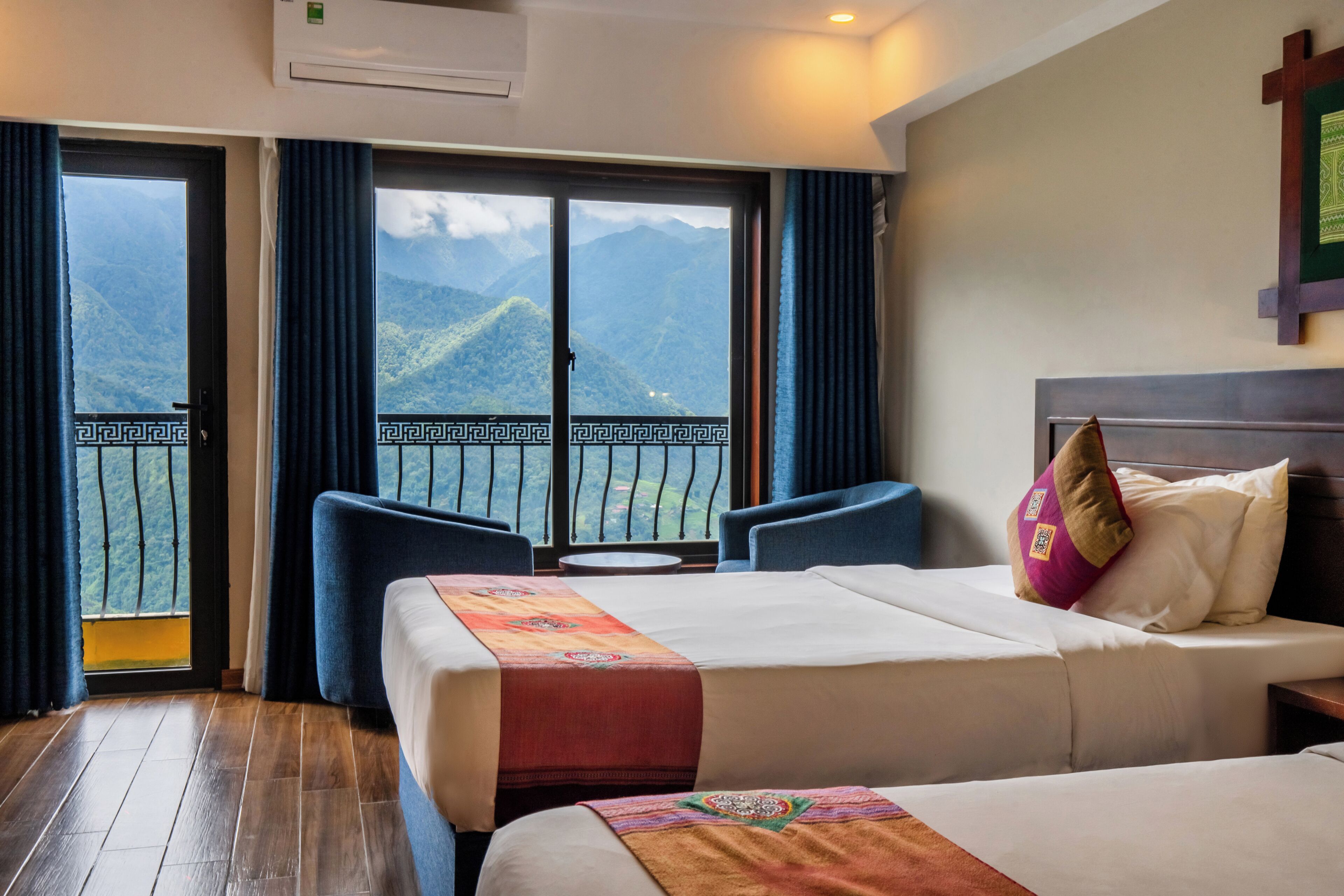 A hotel room with a bed, a sofa, and a balcony with a mountain view.