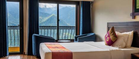 A hotel room with a bed, a sofa, and a balcony with a mountain view.