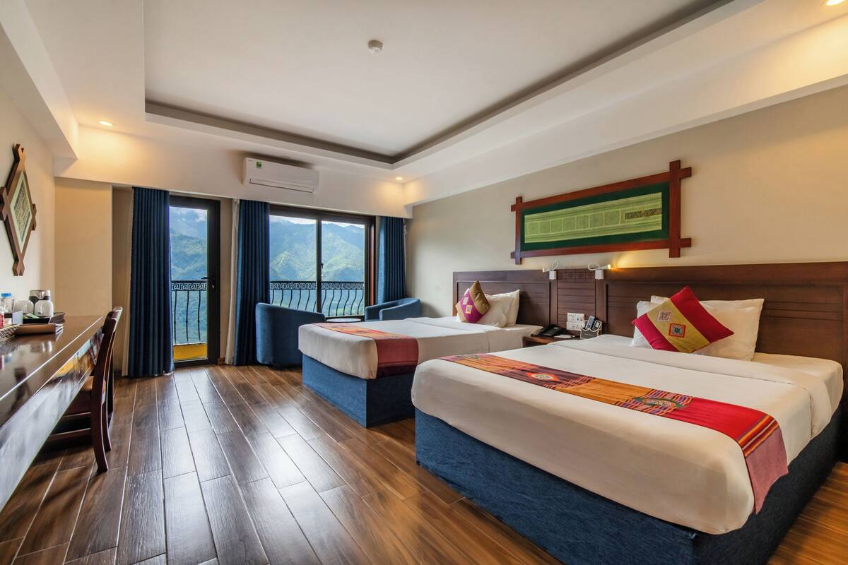 A hotel room with two beds, a desk, and a view of mountains.