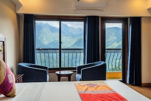 A hotel room with a bed, two armchairs, a small table, and a balcony with a mountain view. - Sapa Charm Hotel (Sa Pa)