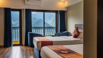 A hotel room with two beds, a balcony with a view of mountains, and a ceiling fan.