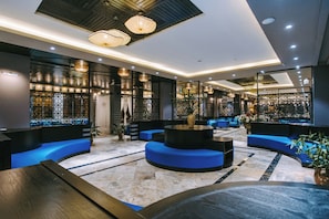 Eine moderne Lobby mit blauen Sitzgelegenheiten, einem runden Tisch in der Mitte und dekorativer Beleuchtung.