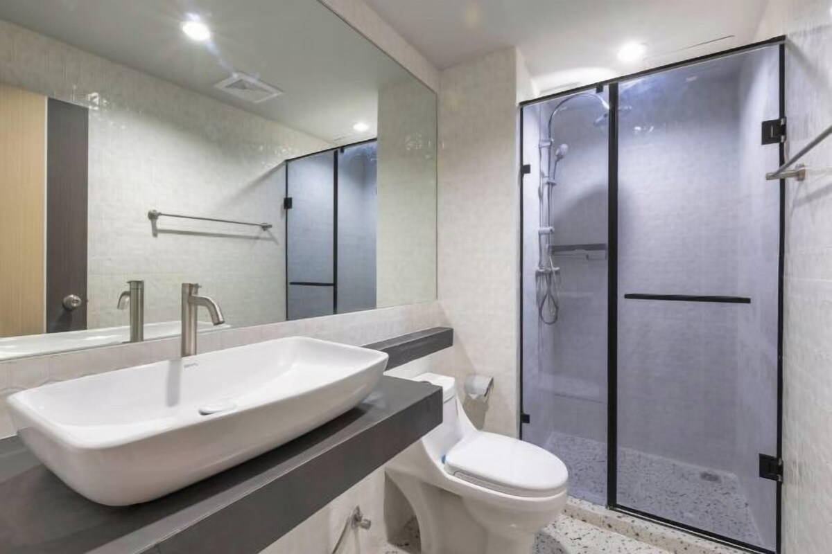 A modern bathroom with a large white sink, a toilet, and a glass-enclosed shower.