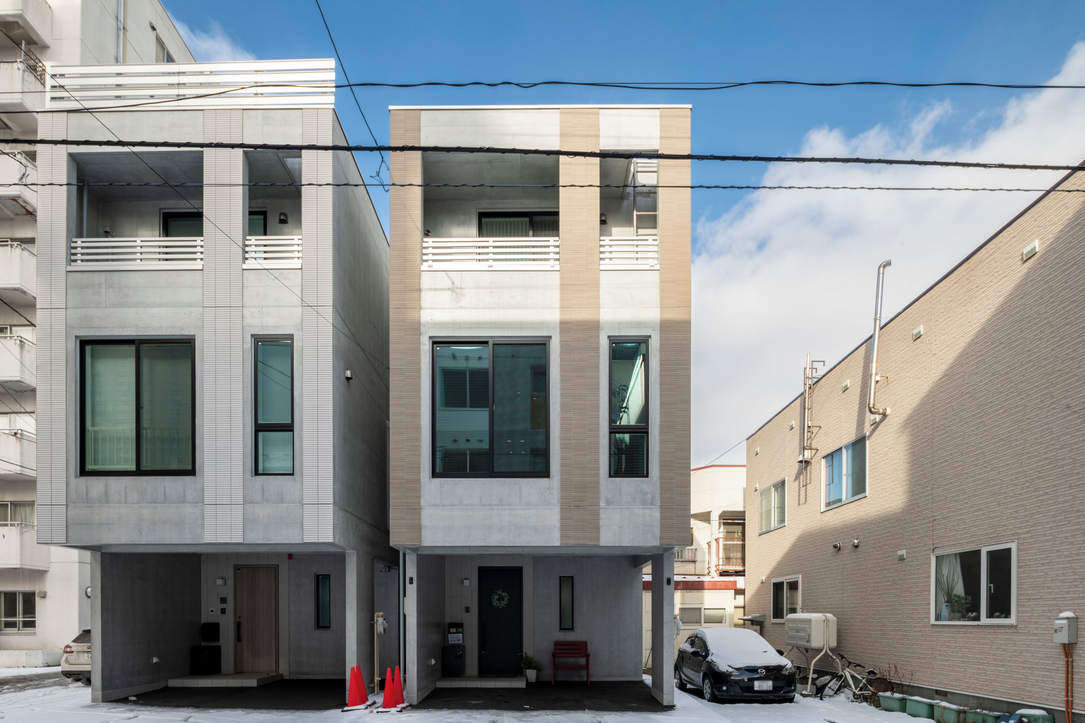 Een modern gebouw met twee verdiepingen, een platte gevel, grote ramen en een klein entreegebied met een bankje en een deur.