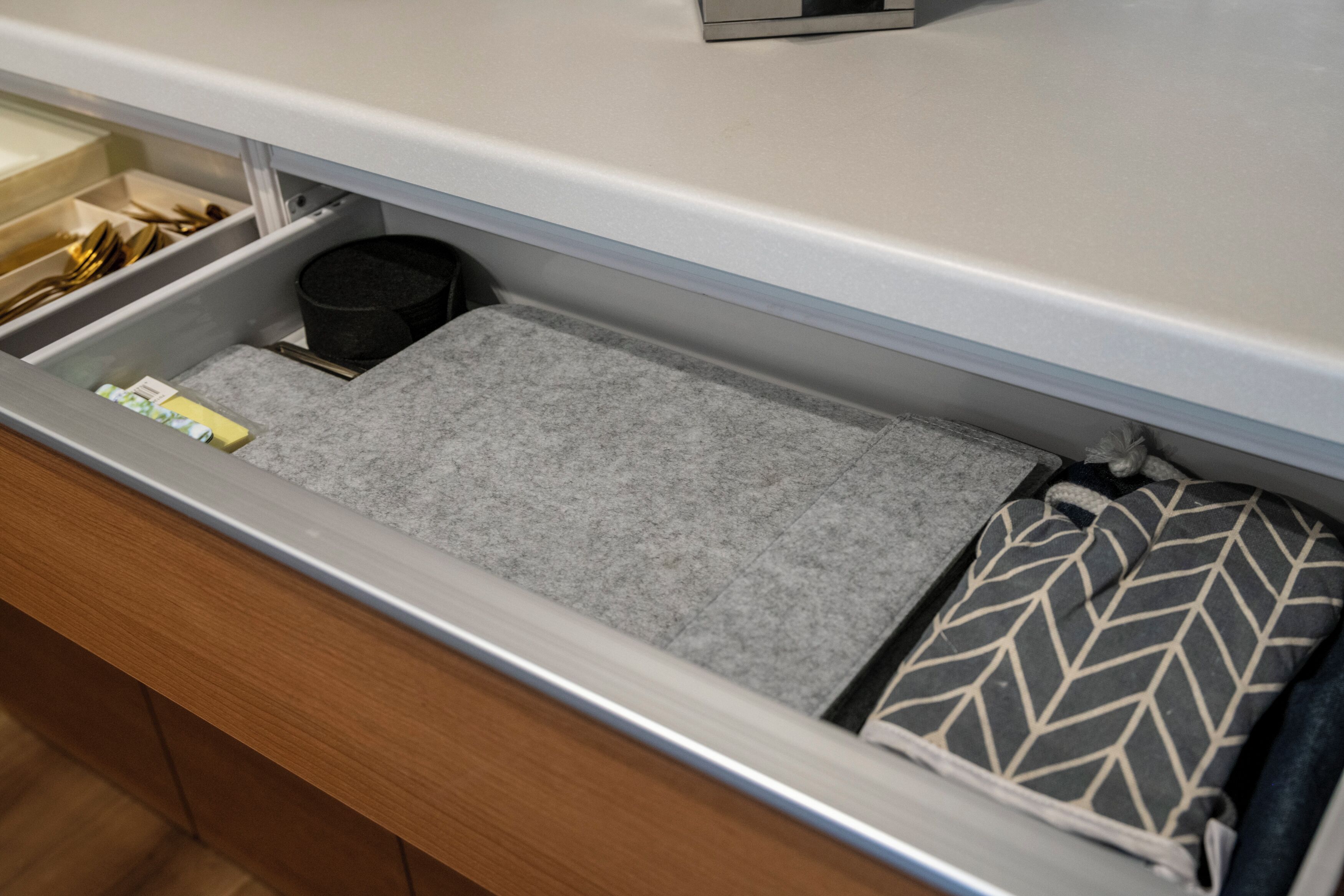 A drawer with a grey felt mat, a black trash bin, and a patterned pillow.