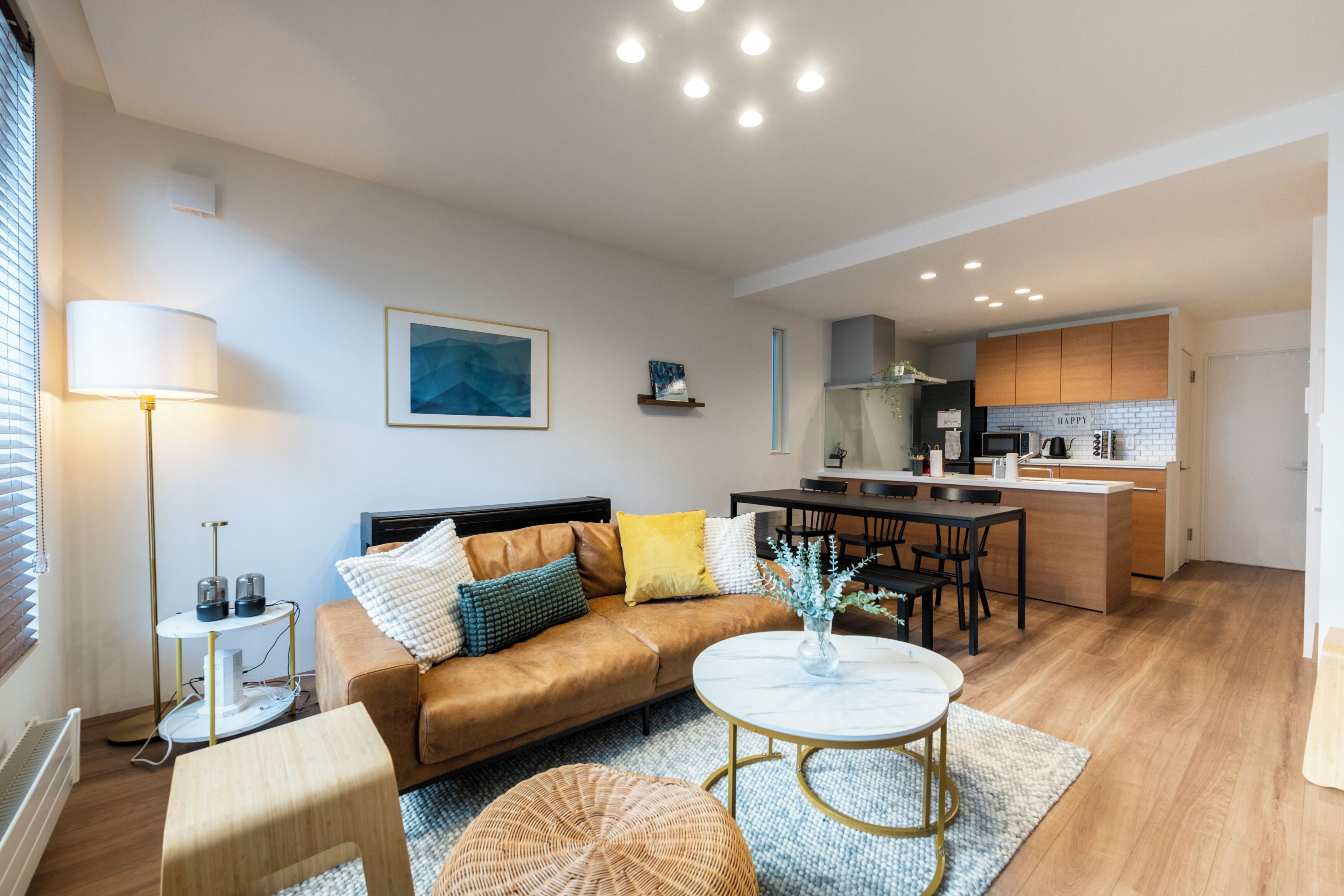 A modern living room with a sofa, coffee table, and a dining area with a kitchen in the background.