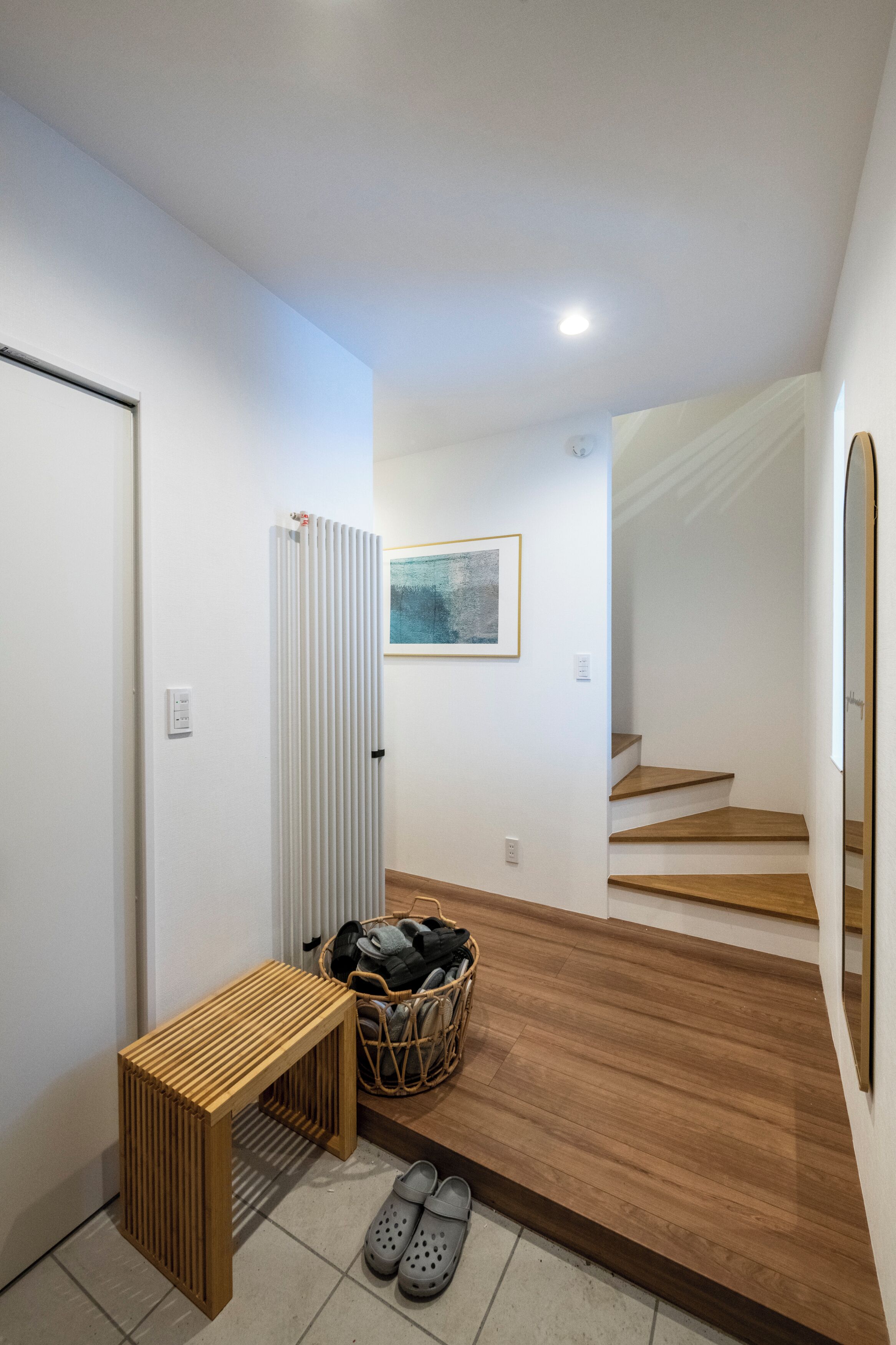 A modern hallway with a wooden bench, a radiator, a wicker basket, and a pair of shoes.