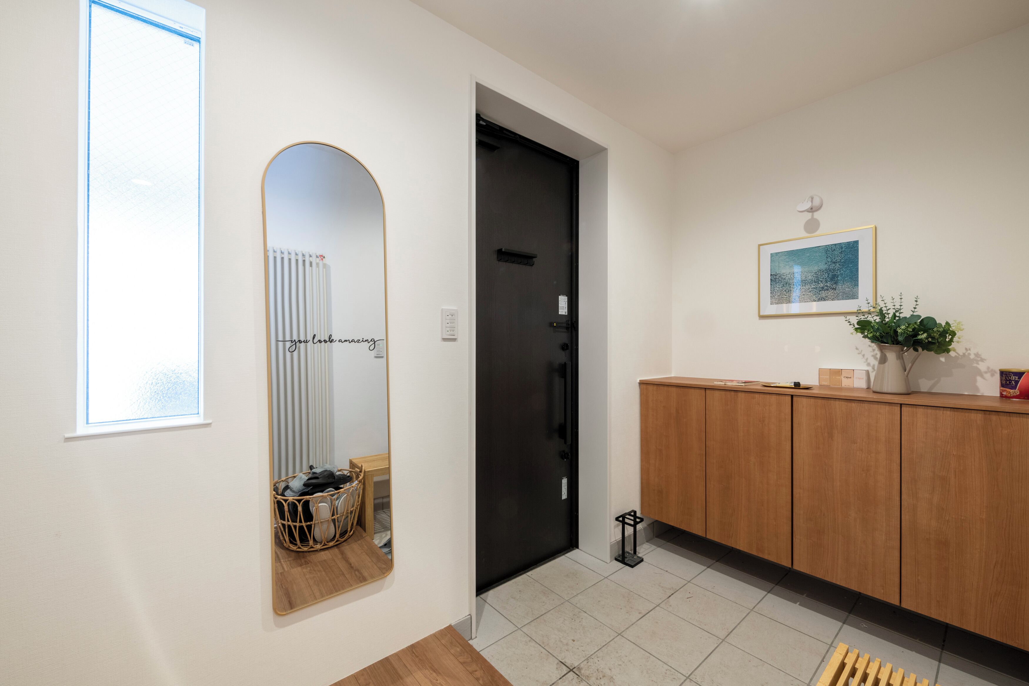 A hallway with a mirror, a black door, a wooden cabinet, and a framed picture on the wall.
