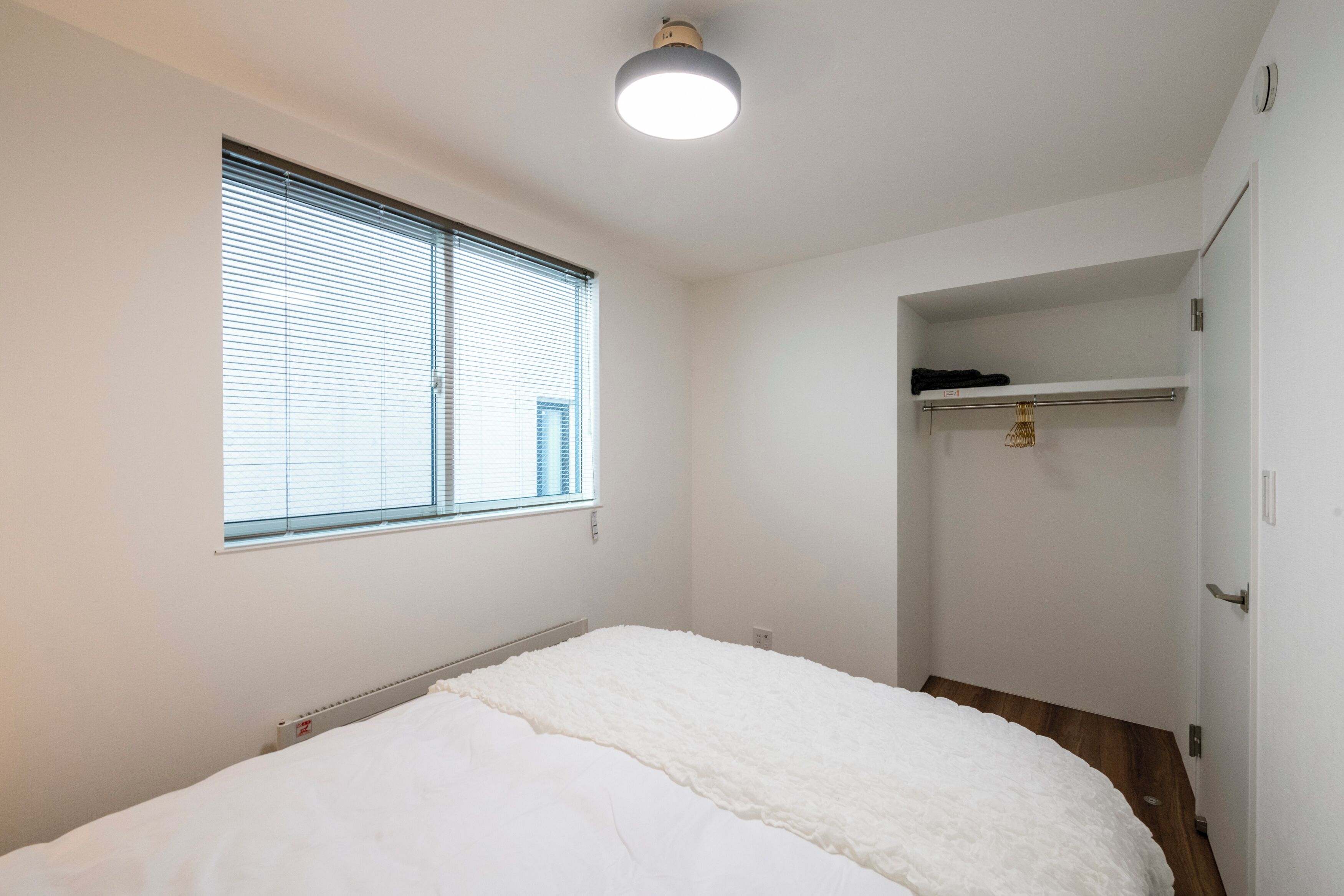 Ein Schlafzimmer mit einem Bett, einem Fenster mit Jalousien, einer Heizung und einem Kleiderschrank.
