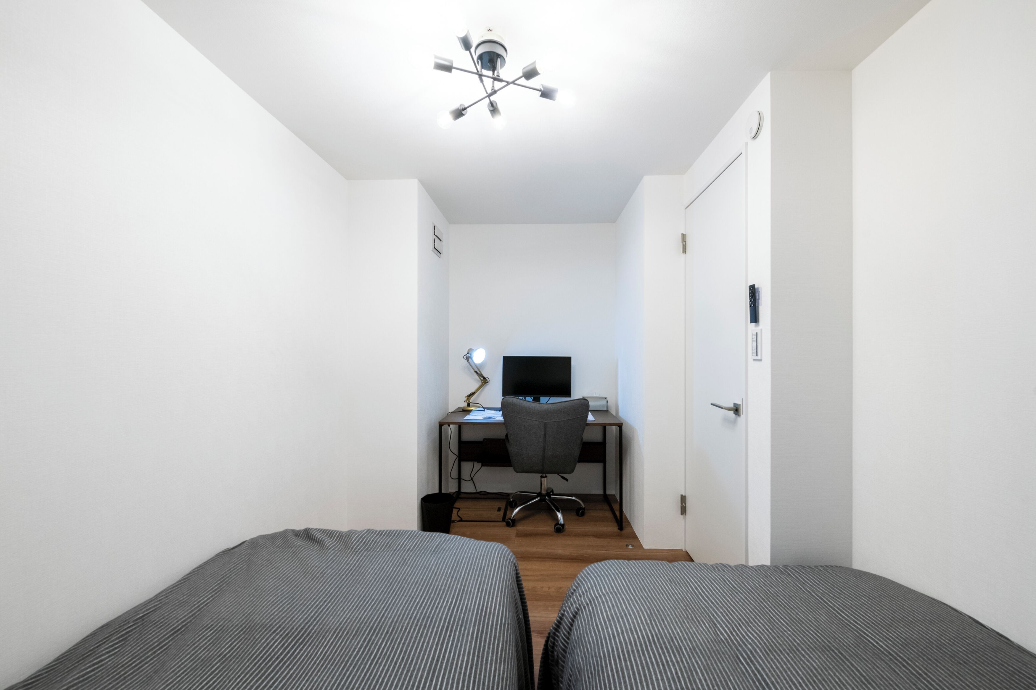 A bedroom with two single beds, a desk with a computer, and a ceiling fan.