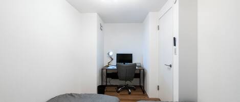 A bedroom with two single beds, a desk with a computer, and a ceiling fan.