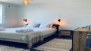 A bedroom with a bed, bedside tables, a nightstand, a lamp, and a hanging light fixture.