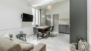 A modern living room with a dining area, a TV mounted on the wall, and a kitchen in the background.