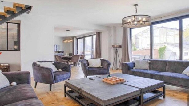 A modern living room with a sofa set, a coffee table, and a dining area in the background.