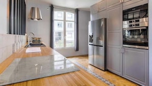 A modern kitchen with stainless steel appliances, a large window, and a wooden floor.