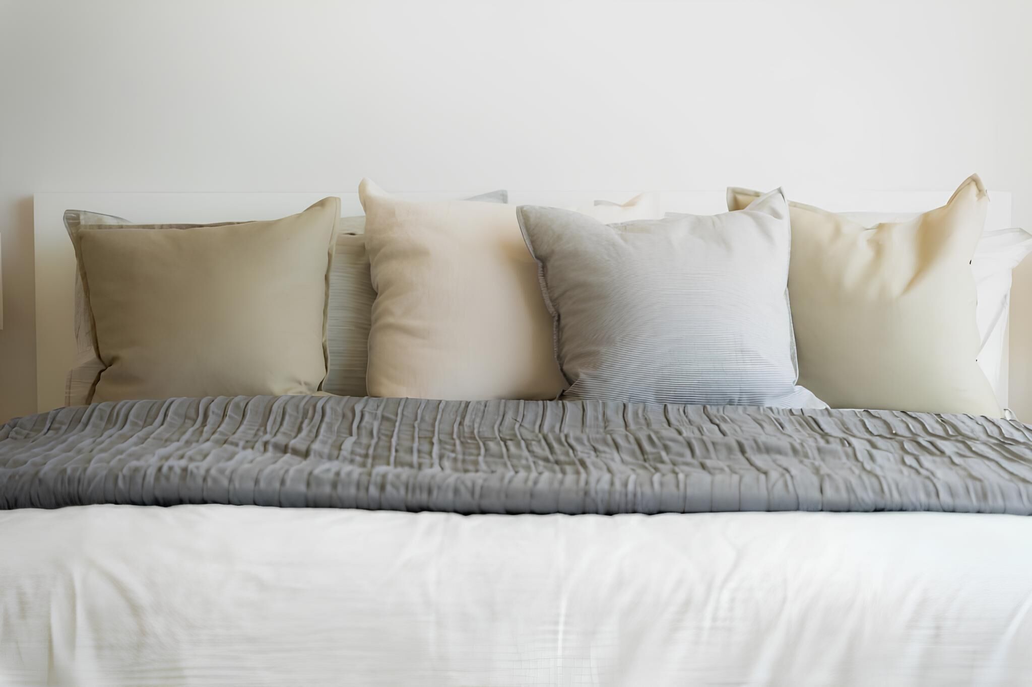 A bed with a grey quilt and three pillows in a neutral color palette.