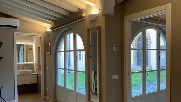 A spacious room with a large bed, a bathroom with a sink, and arched windows offering a view of the outdoors. - Inside Lucca  Walls, Historic Home,  private Garden, Terrace (Lucca)