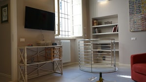 A living room with a TV mounted on the wall, a radiator, a bookshelf, and a red armchair. - Inside Lucca  Walls, Historic Home,  private Garden, Terrace (Lucca)