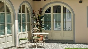 A patio with a table and chairs, surrounded by large arched windows and a potted plant. - Inside Lucca  Walls, Historic Home,  private Garden, Terrace (Lucca)