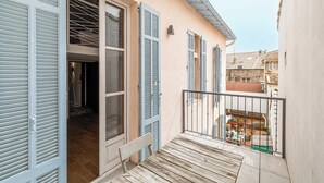 Un balcon doté d’un plancher en bois, d’une rambarde en métal et offrant une vue sur une cour intérieure avec une table et des chaises.