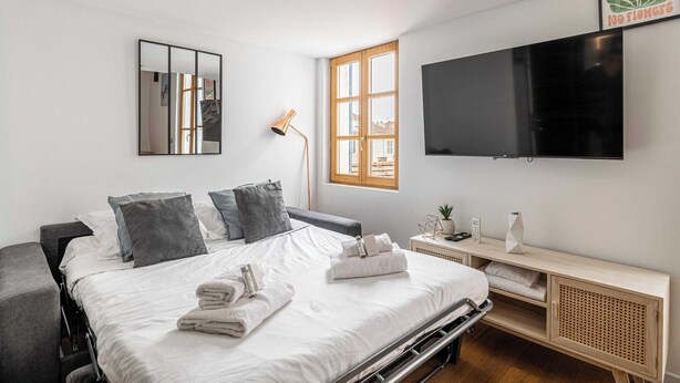 Une chambre d’hôtel moderne dotée d’un grand lit, d’un téléviseur à écran plat, d’une table de chevet avec une lampe et d’une fenêtre donnant sur des immeubles.