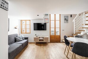 A modern living room with a grey sofa, a TV mounted on the wall, a wooden cabinet, and a dining area with a white table and chairs. - Magnificent Duplex - Meynadier Cannes Center (Cannes)
