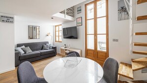 Un salon moderne avec un canapé gris, une table à manger ronde et un téléviseur fixé au mur.