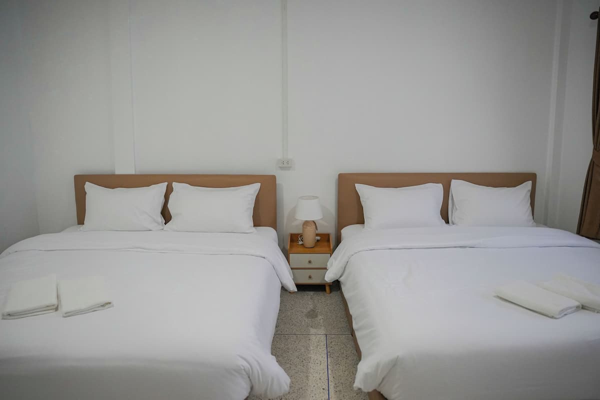 A hotel room with two single beds, each with white bedding and pillows, a wooden headboard, and a nightstand with a lamp and a small table.