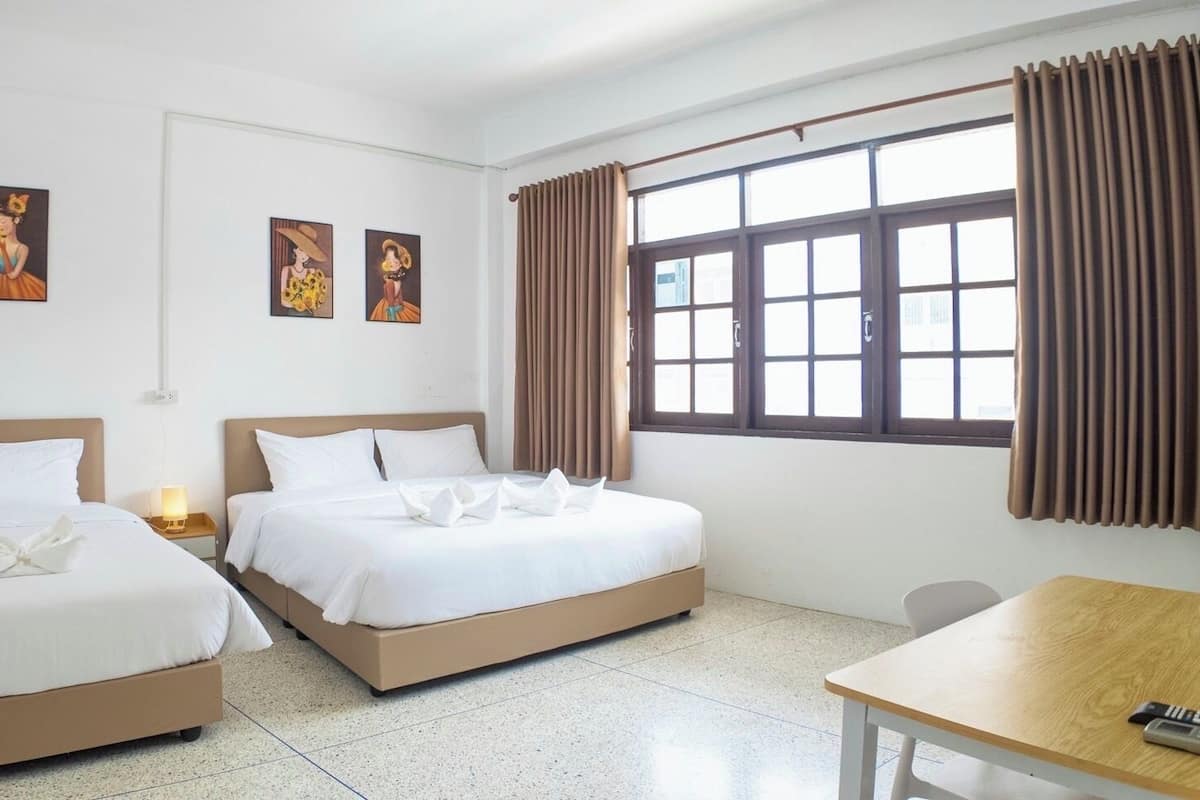 A hotel room with two beds, a wooden table, and a window with curtains.