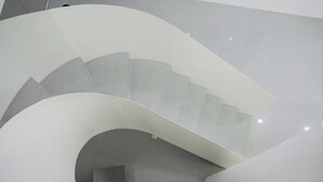 Un escalier en colimaçon au design moderne, réalisé avec des matériaux blancs et doté d’une rampe en verre.