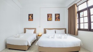 Une chambre d’hôtel avec deux lits, du linge de lit blanc et une table de chevet avec une lampe. Deux tableaux encadrés sont accrochés au mur.