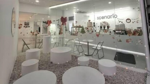 Un intérieur moderne avec des tables et des chaises rondes, un mur de verre orné de décorations et une enseigne indiquant « scénario ».