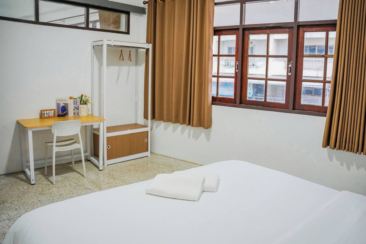 A hotel room with a bed, a desk with a chair, a wardrobe, and a window with curtains.