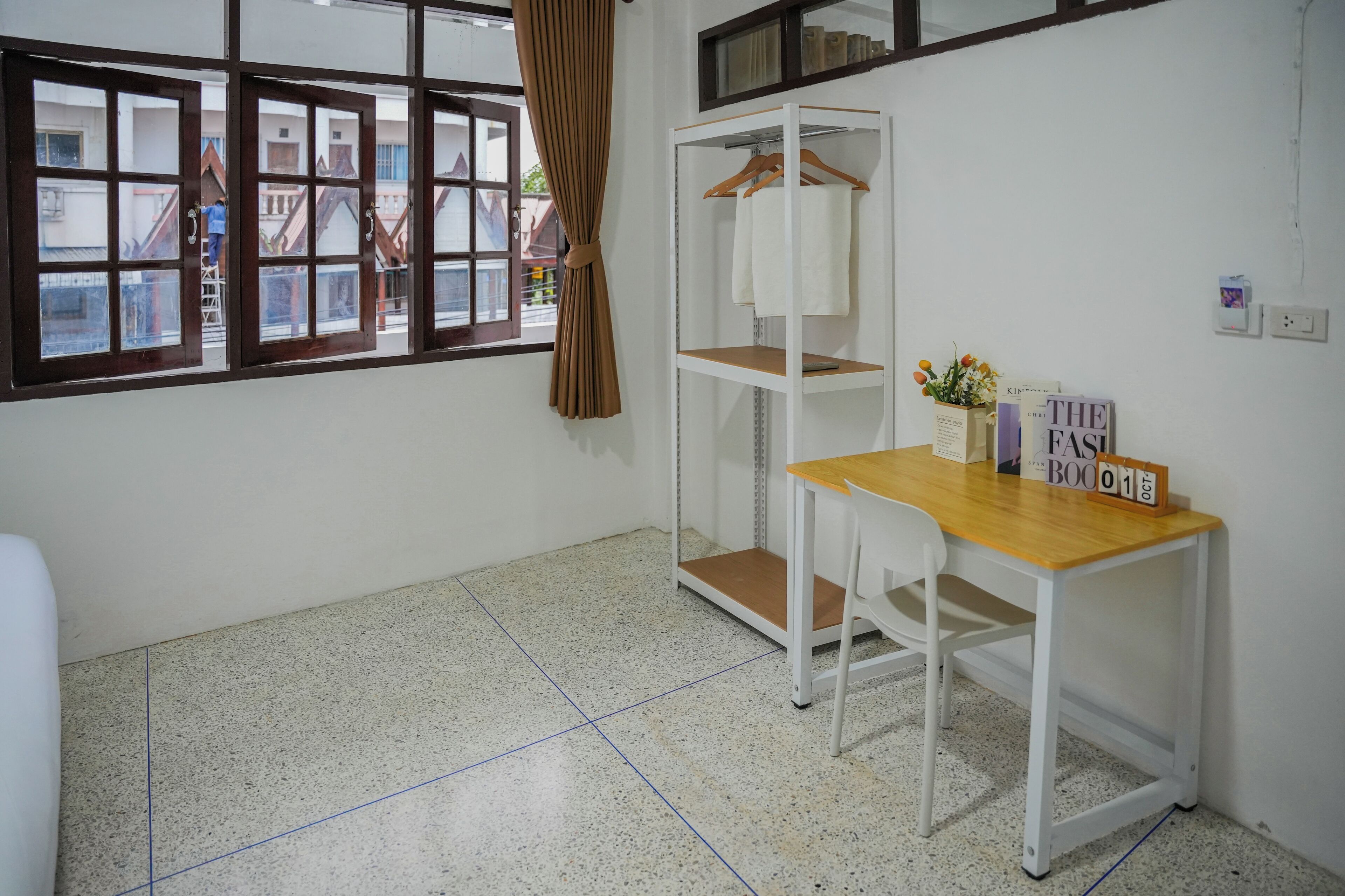 A room with a window, a desk with a chair, a wardrobe, and a shelf with books and a vase.