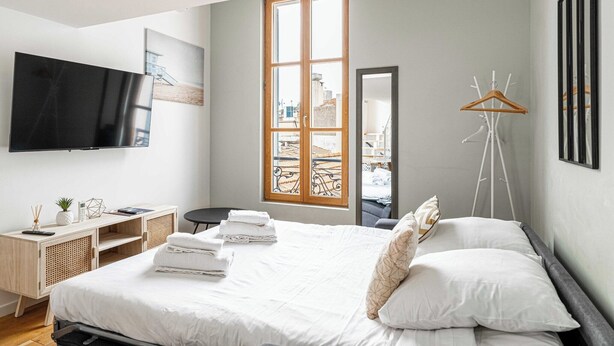 Une chambre d’hôtel moderne équipée d’un lit, d’un bureau, d’une télévision, d’une fenêtre avec vue et d’un porte-manteau.