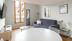 Un salon moderne avec un canapé gris, une table ronde blanche et un téléviseur fixé au mur.