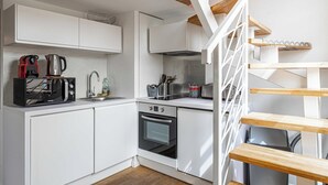 Une cuisine moderne avec des meubles blancs, un four encastré, une machine à café et une bouilloire.