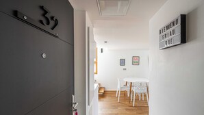 Un intérieur moderne avec une porte gris foncé portant le numéro 32, un coin repas blanc avec une table ronde et des chaises, et un panneau d’accueil sur le mur.