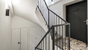 Una escalera moderna con barandillas negras, una puerta oscura con el número 13 y un suelo con diseño.