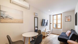 Una sala de estar moderna con un sofá negro, dos sillones grises, una mesa blanca y un televisor en la pared.