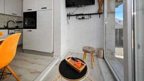 A modern kitchen with white cabinets, a black TV mounted on the wall, and a dining area with a wooden table and orange chairs. - DaLaPaDo by Interhome (Zadar)